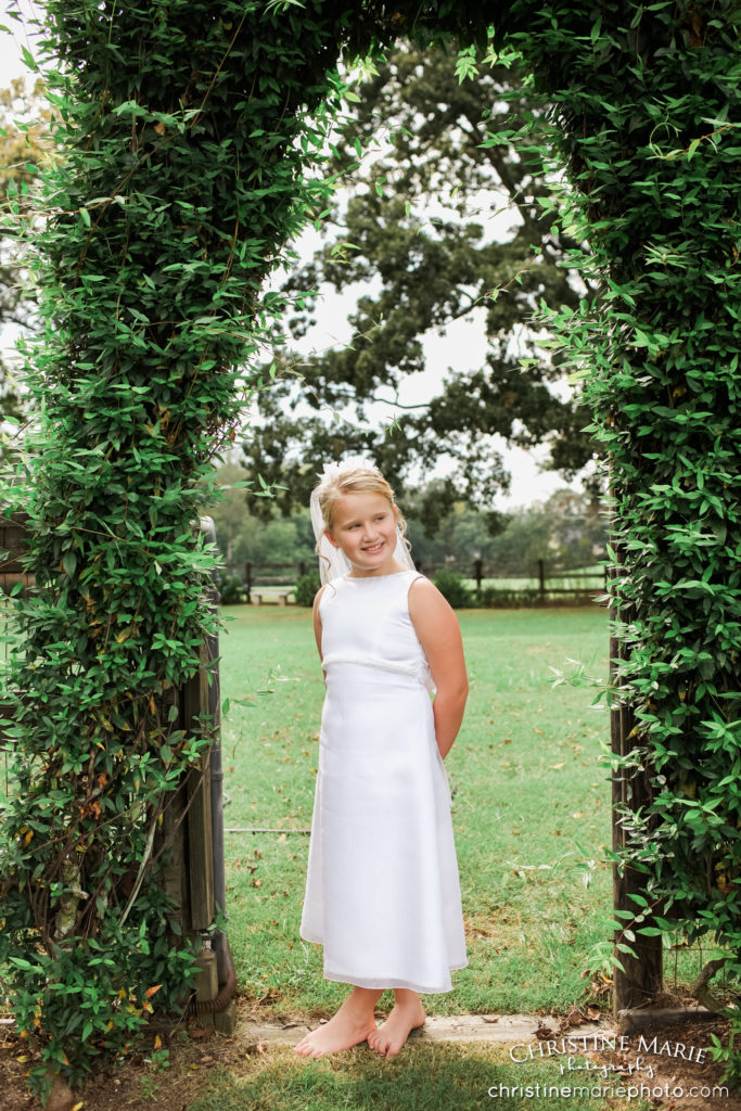 little girl in first holy communion dress under ivy arch 