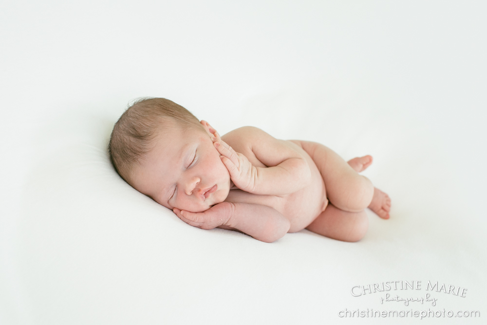 side laying newborn baby with hands on cheeks 