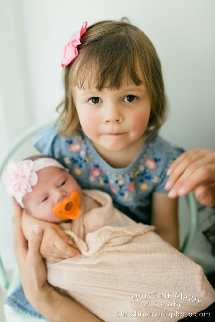 toddler big sis holding newborn baby sister 