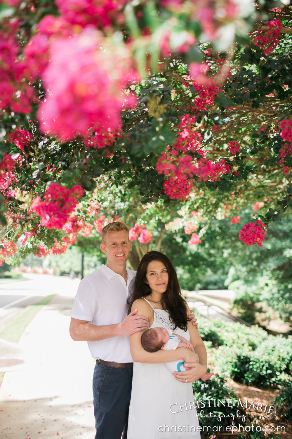 gorgeous couple holding new baby under flowering pink tree