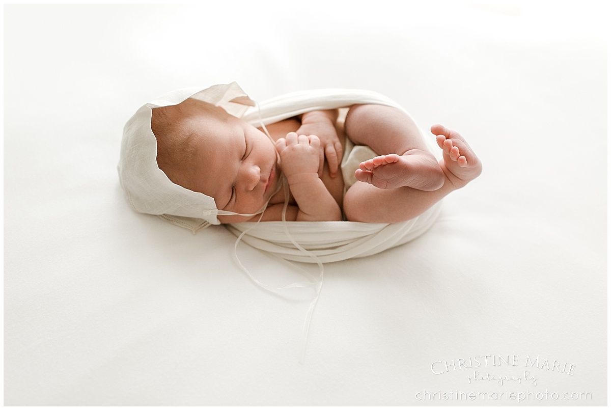 sweet sleepy newborn baby boy on white with bonnet