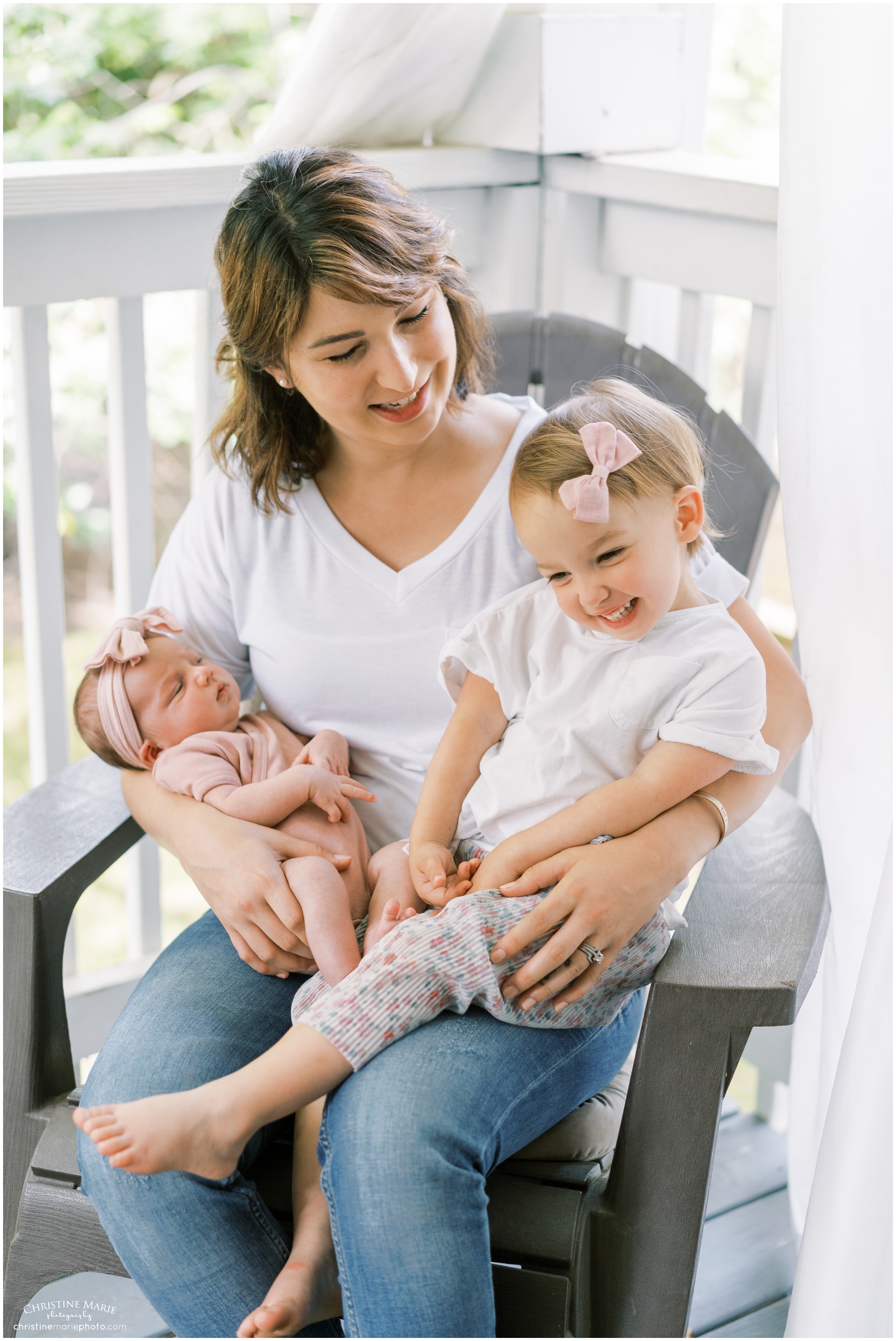 mom holding two girls on her lap in lifestyle newborn session