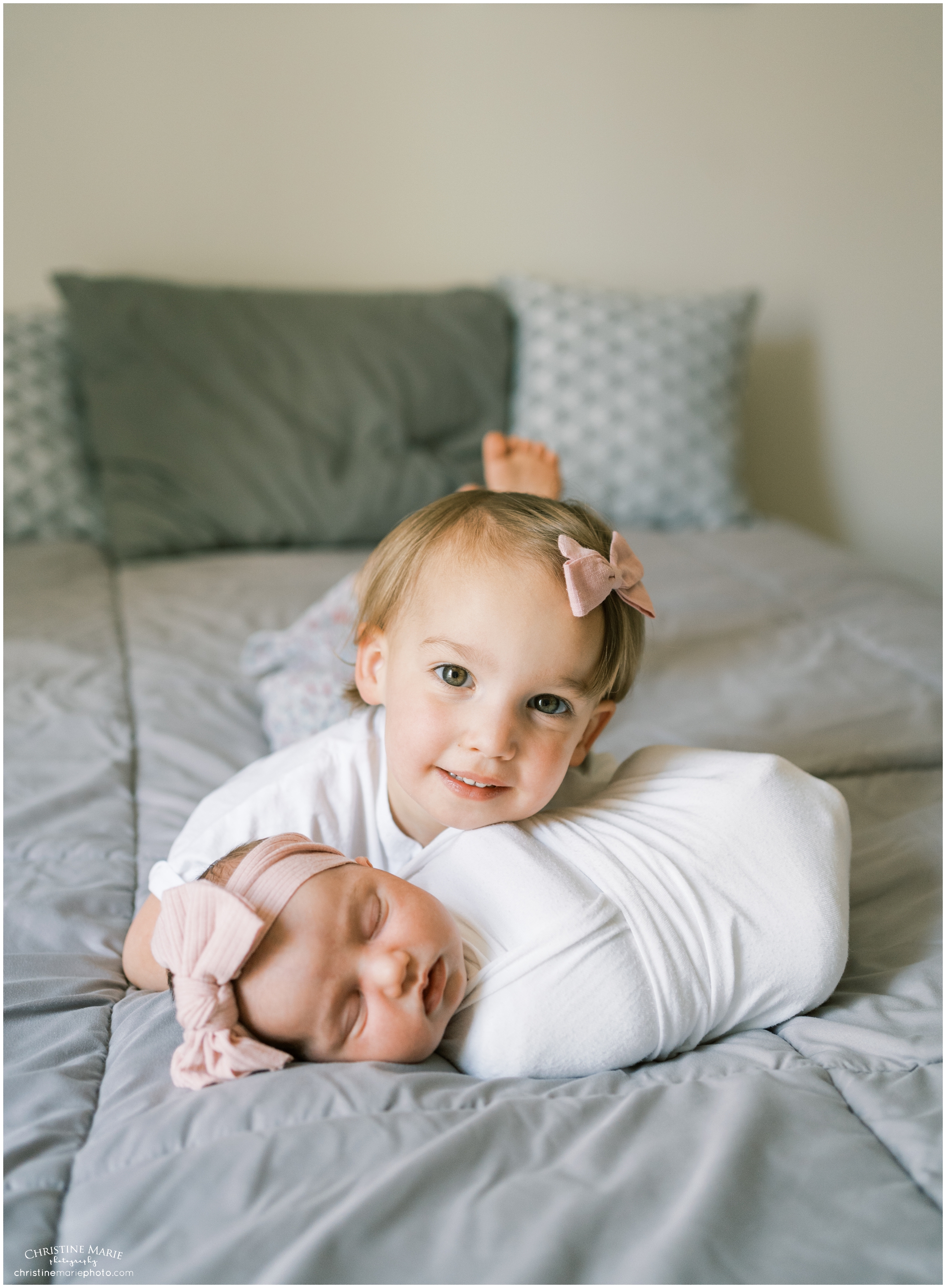 toddler big sis laying on bed with newborn little sister