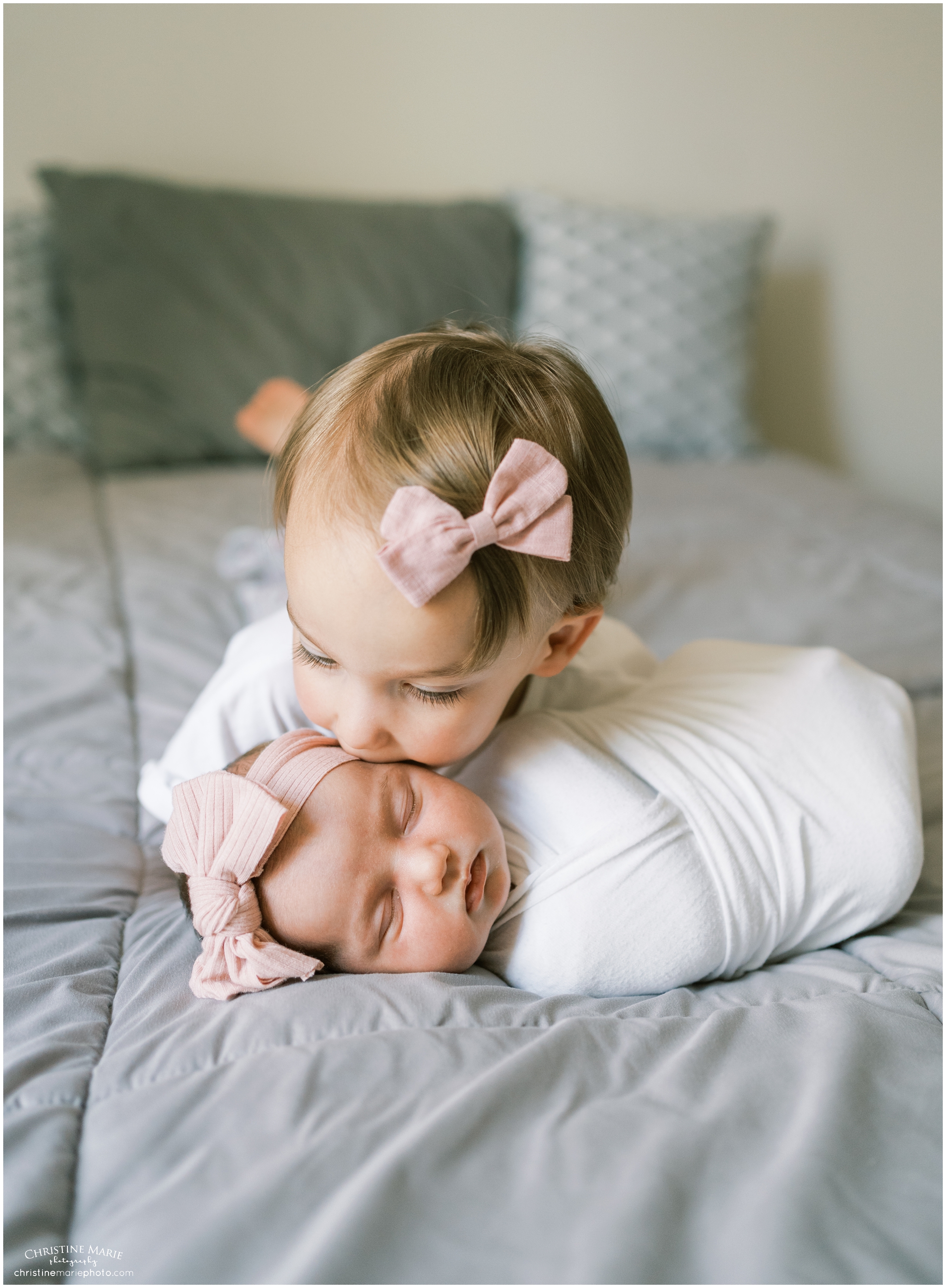 toddler big sis kissing newborn baby sis on bed
