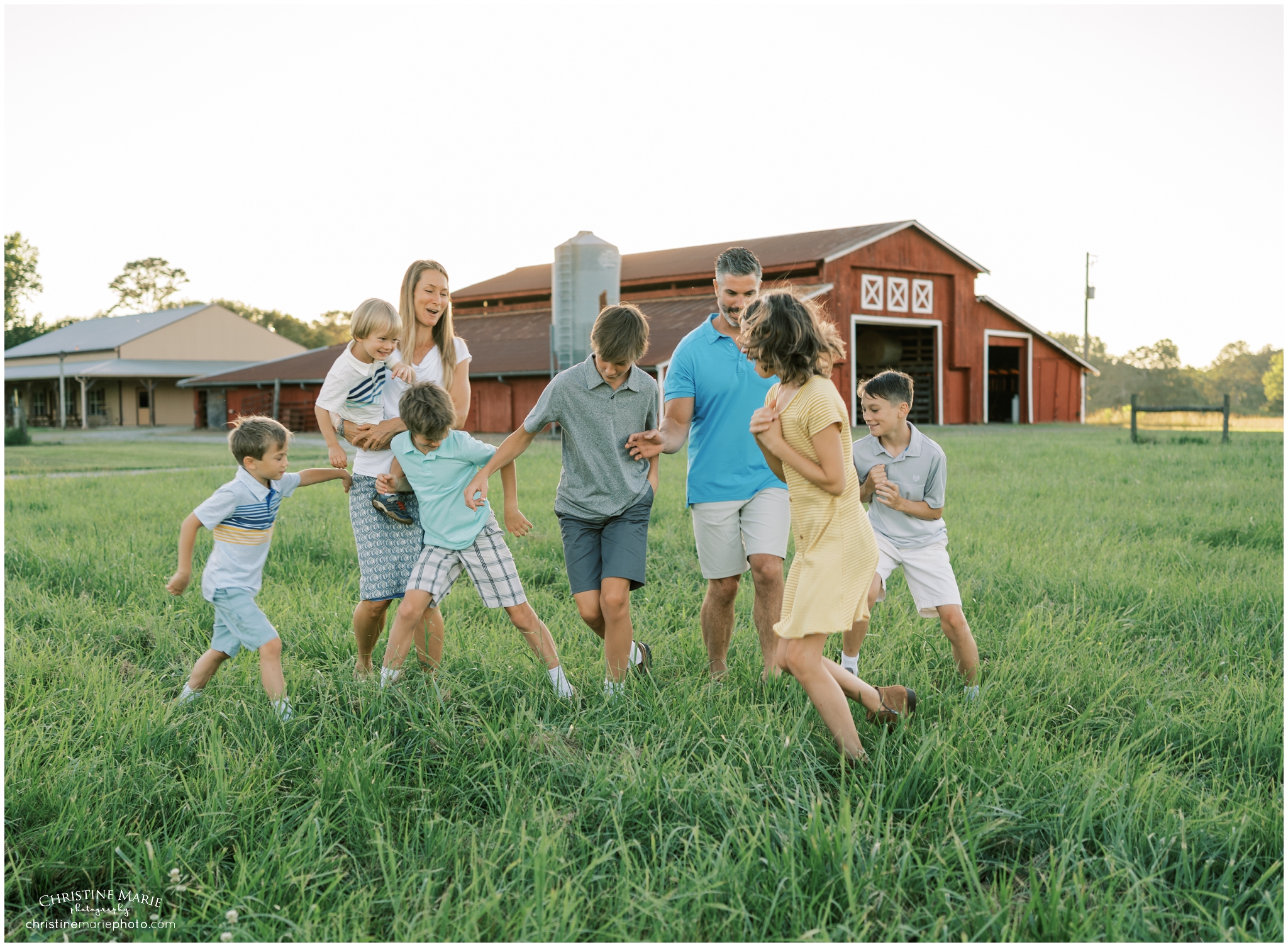 large family playing in a field with red barn in cumming ga