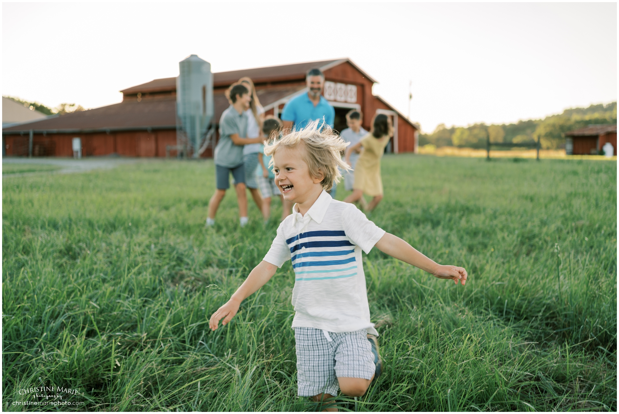 little boy playing in a field with red barn in cumming ga