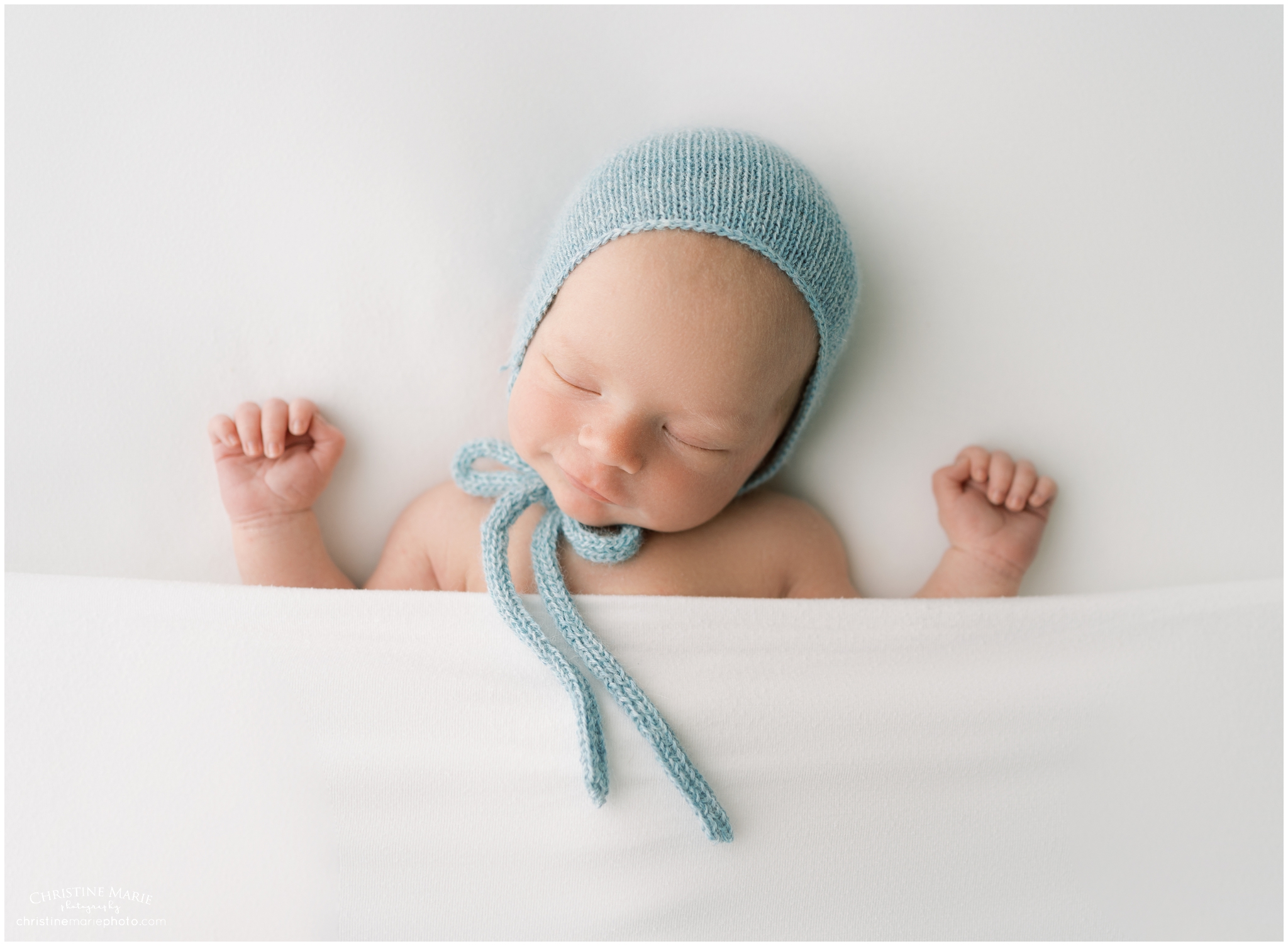 smiling newborn baby boy all tucked in a white bed sheet