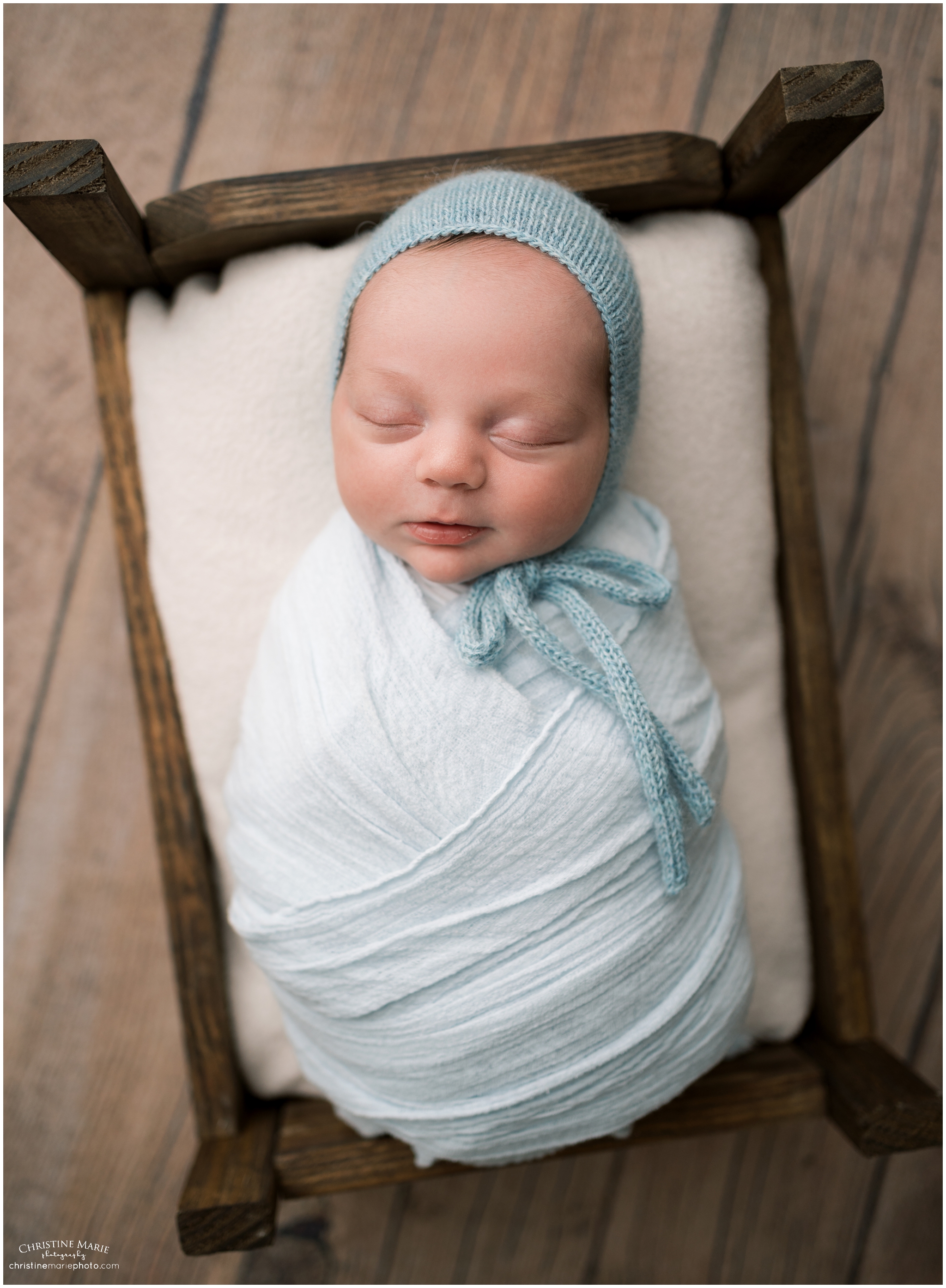 baby boy in bonnet sleeping on tiny wooden bed