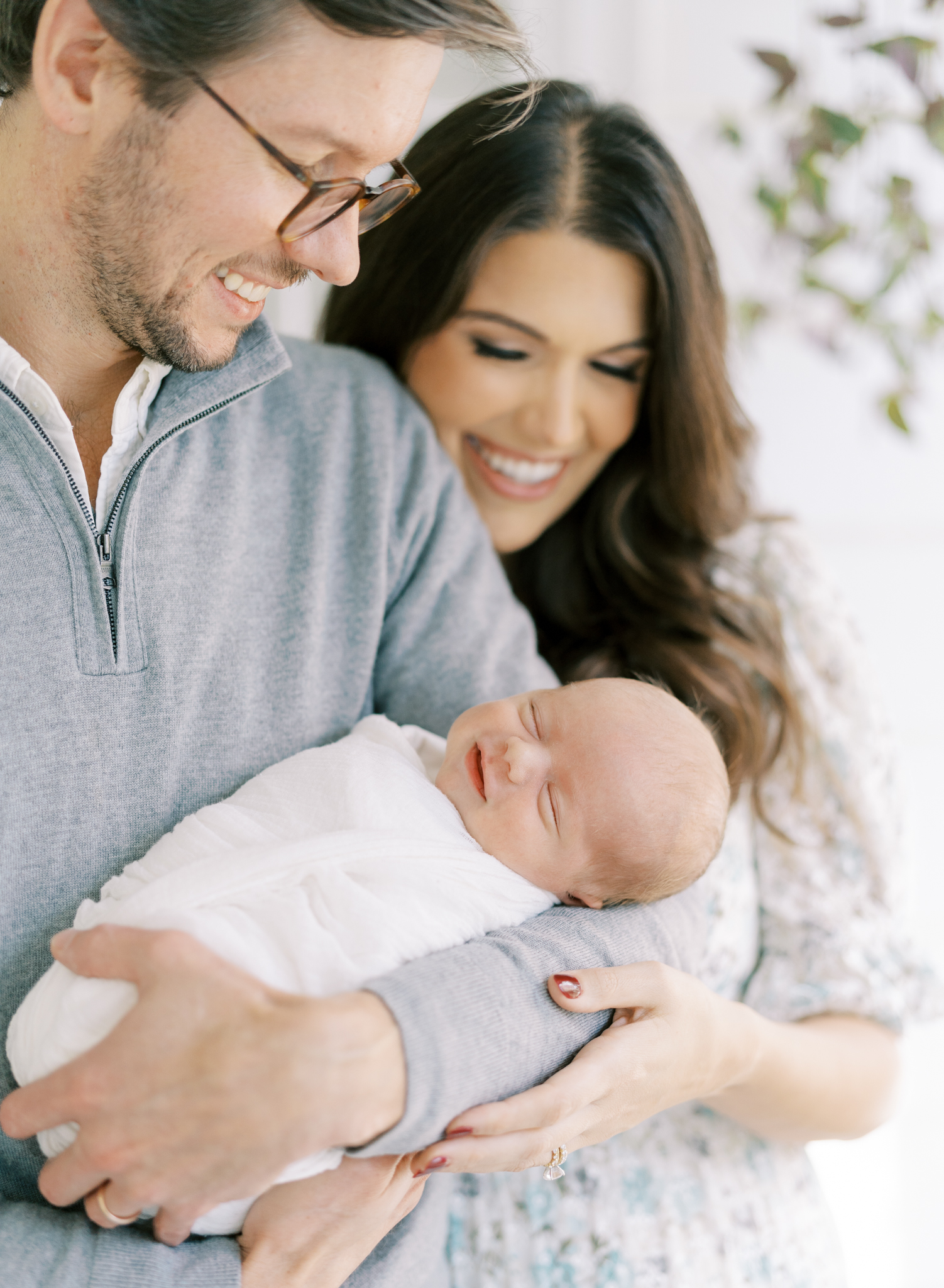 Newborn baby boy smiling in the arms of his parents during photoshoot in Atlanta.