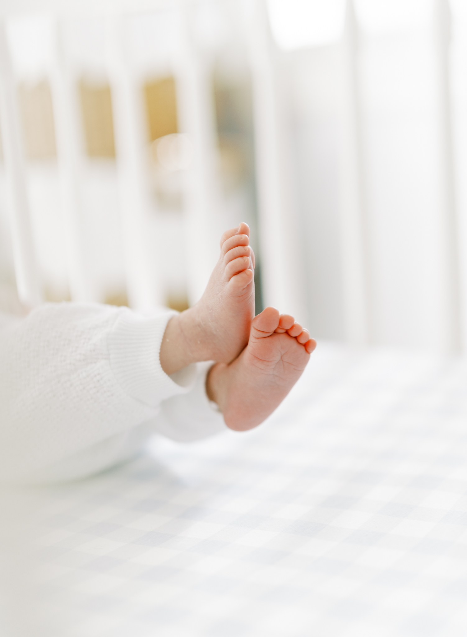 Tiny newborn feet kicking around in crib with plaid sheets