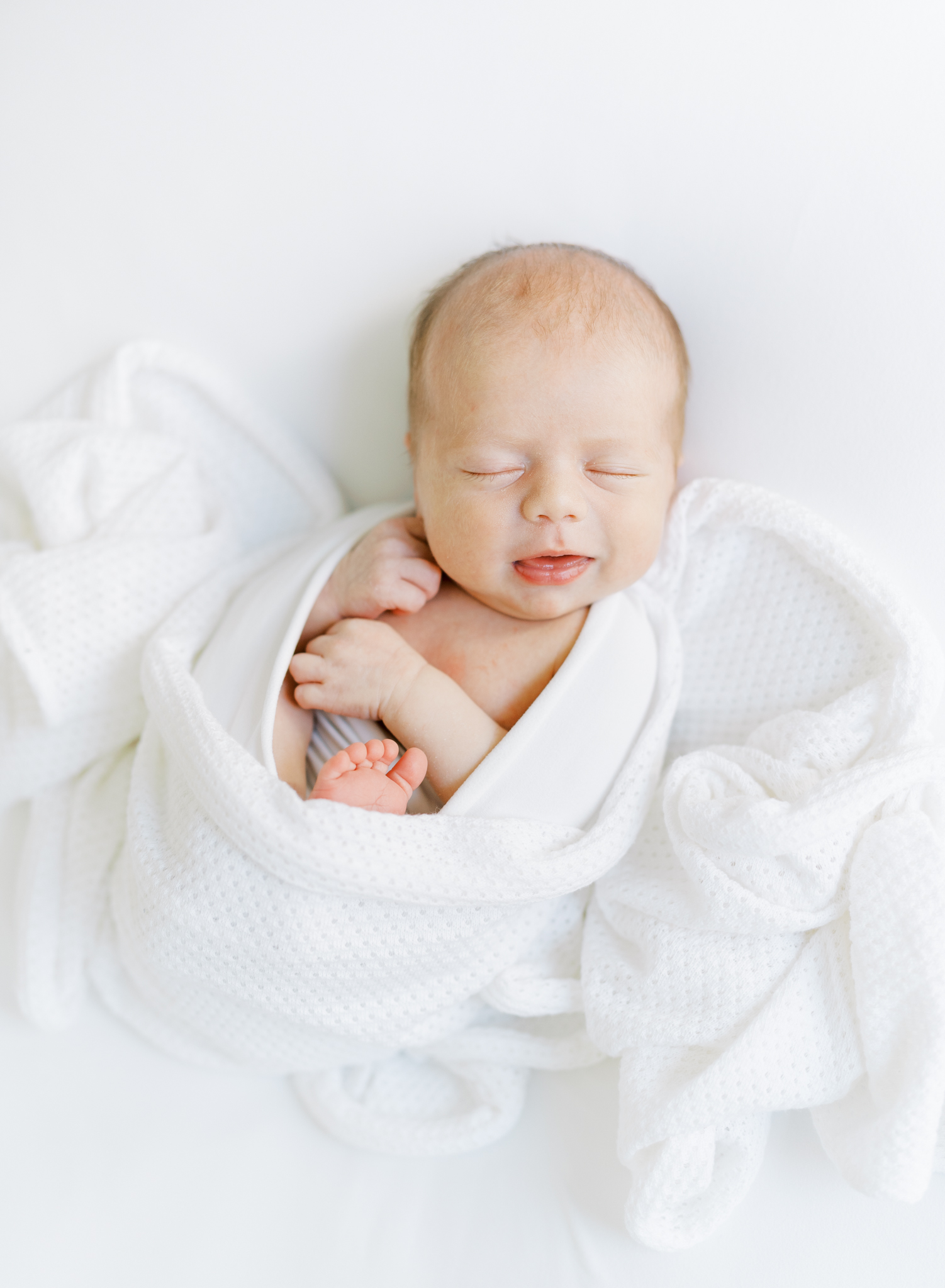 Newborn boy snuggled up in all white for photoshoot.
