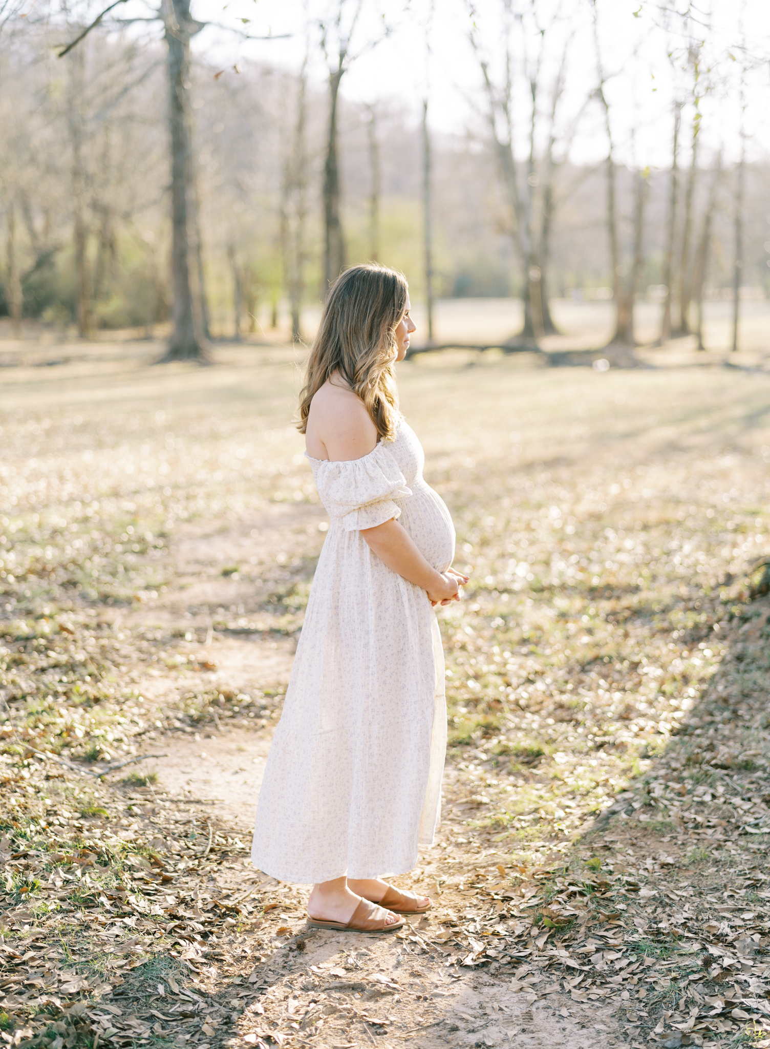 Pregnant woman standing in the glow of teh winter sun in an open field in Cumming, GA