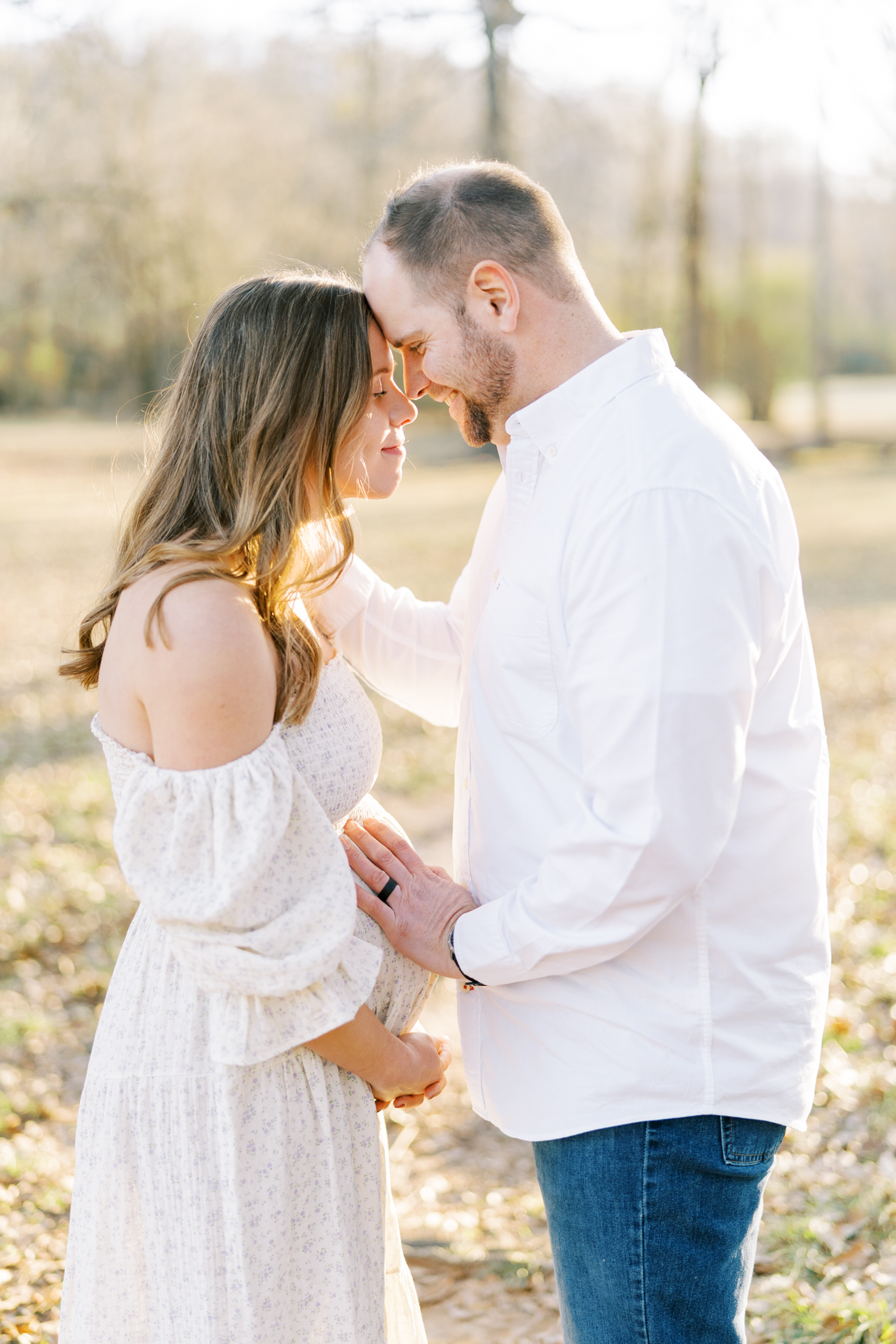 Expectant couple with foreheads together standing in the glow of the winter sunset