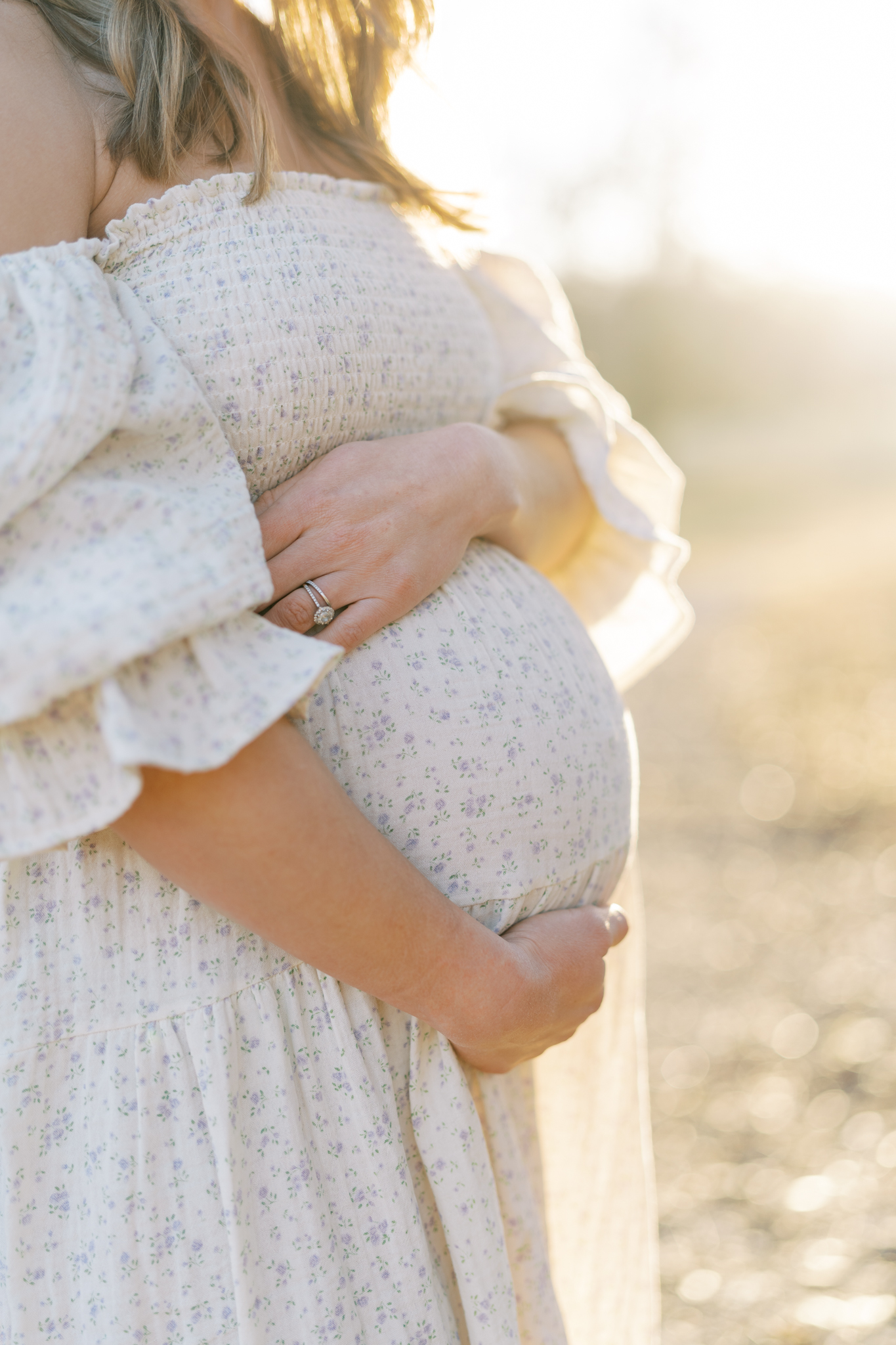 close up of woman's arms hugging her pregnant belly basking in soft hazy winter lighting