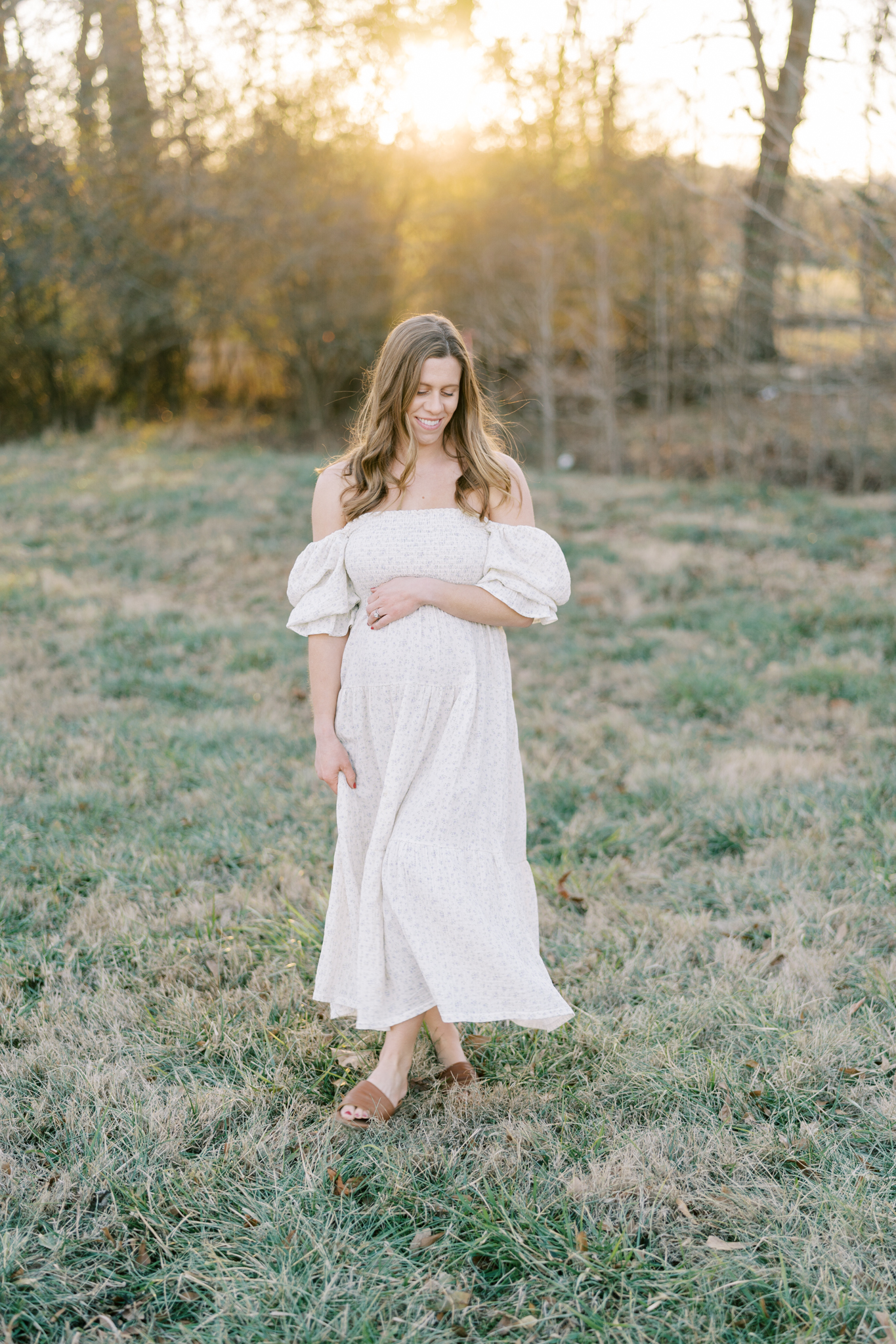 Pregnant woman in dress walking in a field at sunset
