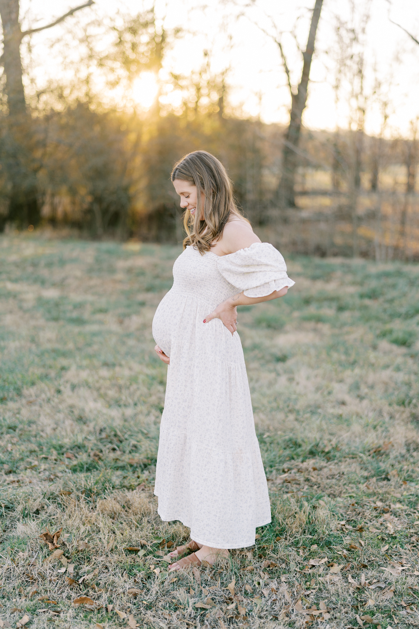 Pregnant mom looking down at her belly in a sunset field