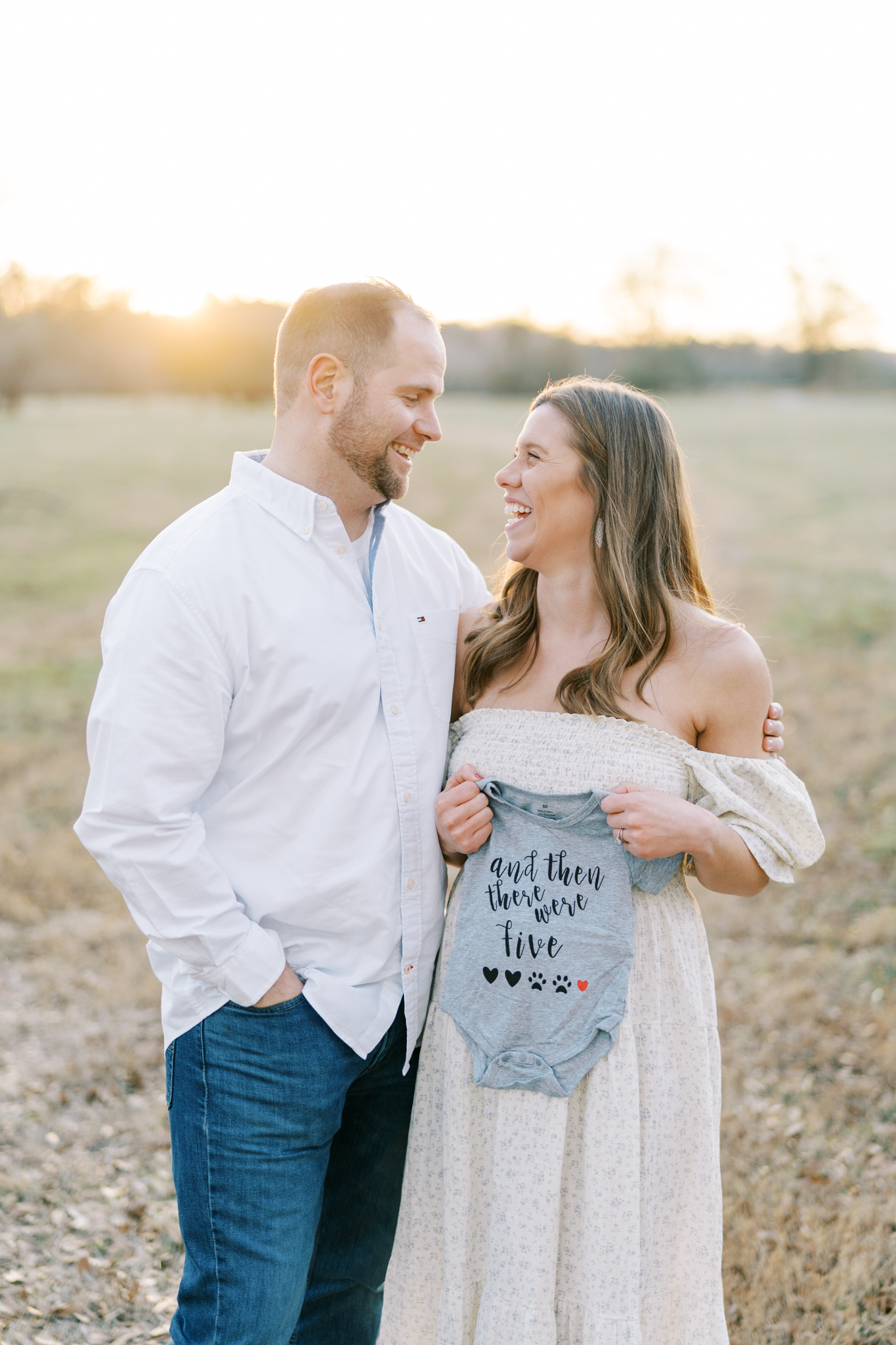Happy expectant couple holding up a onsie baby announcement in Cumming GA