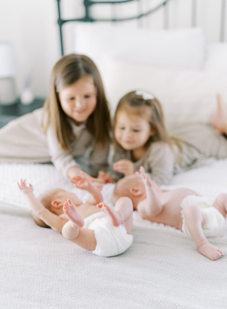 siblings looking at their newborn twin brother and sister on a bed