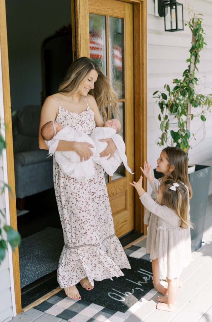 Mom walking out the door of her country home holding newborn twins with other children around her