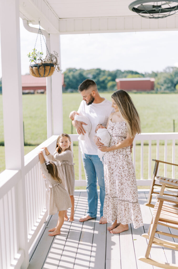 Family with newborn twins and other kids hanging out on front porch with farm view