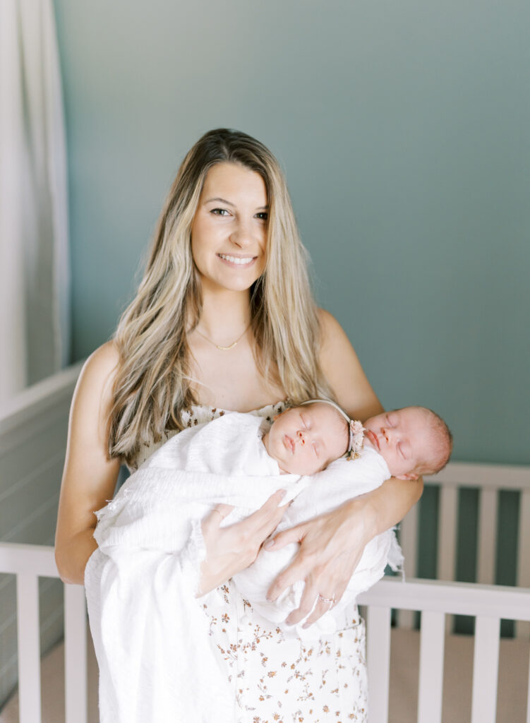 Beautiful mom holding her her twin newborn babies in her arms.