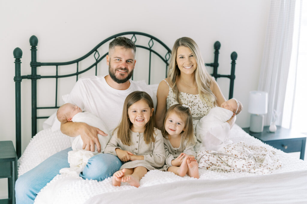 Family with 4 kids and newborn twins posed on a bed for lifestyle newborn photos in Cumming, GA