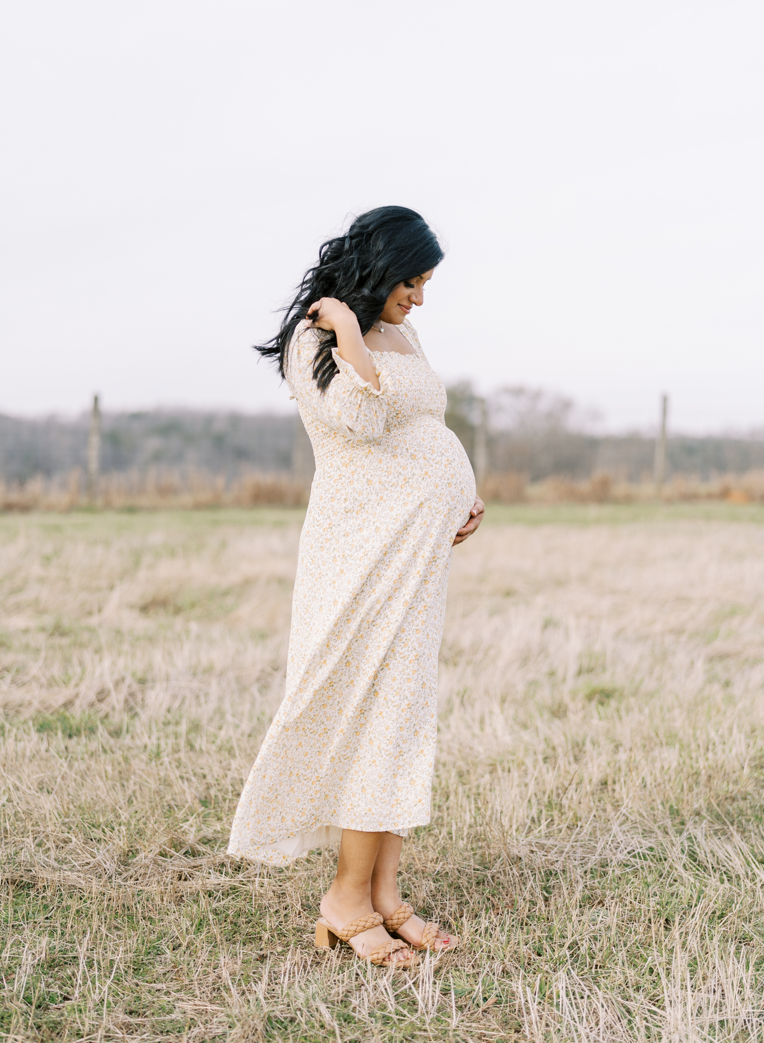 pregnant mom looking down at belly in a field as the wind blows her dress and hair