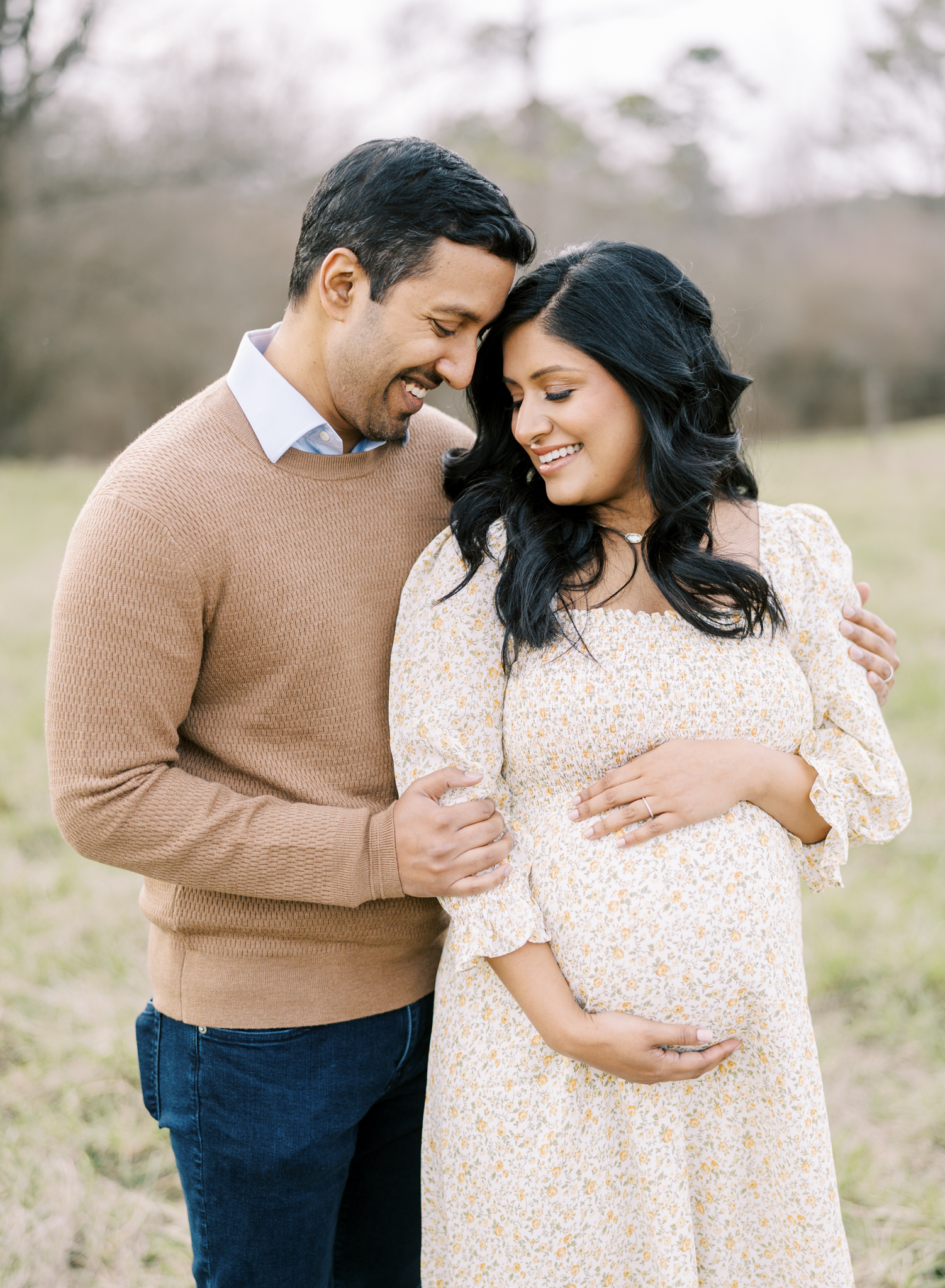 expecting parents smiling towards each other in a field 