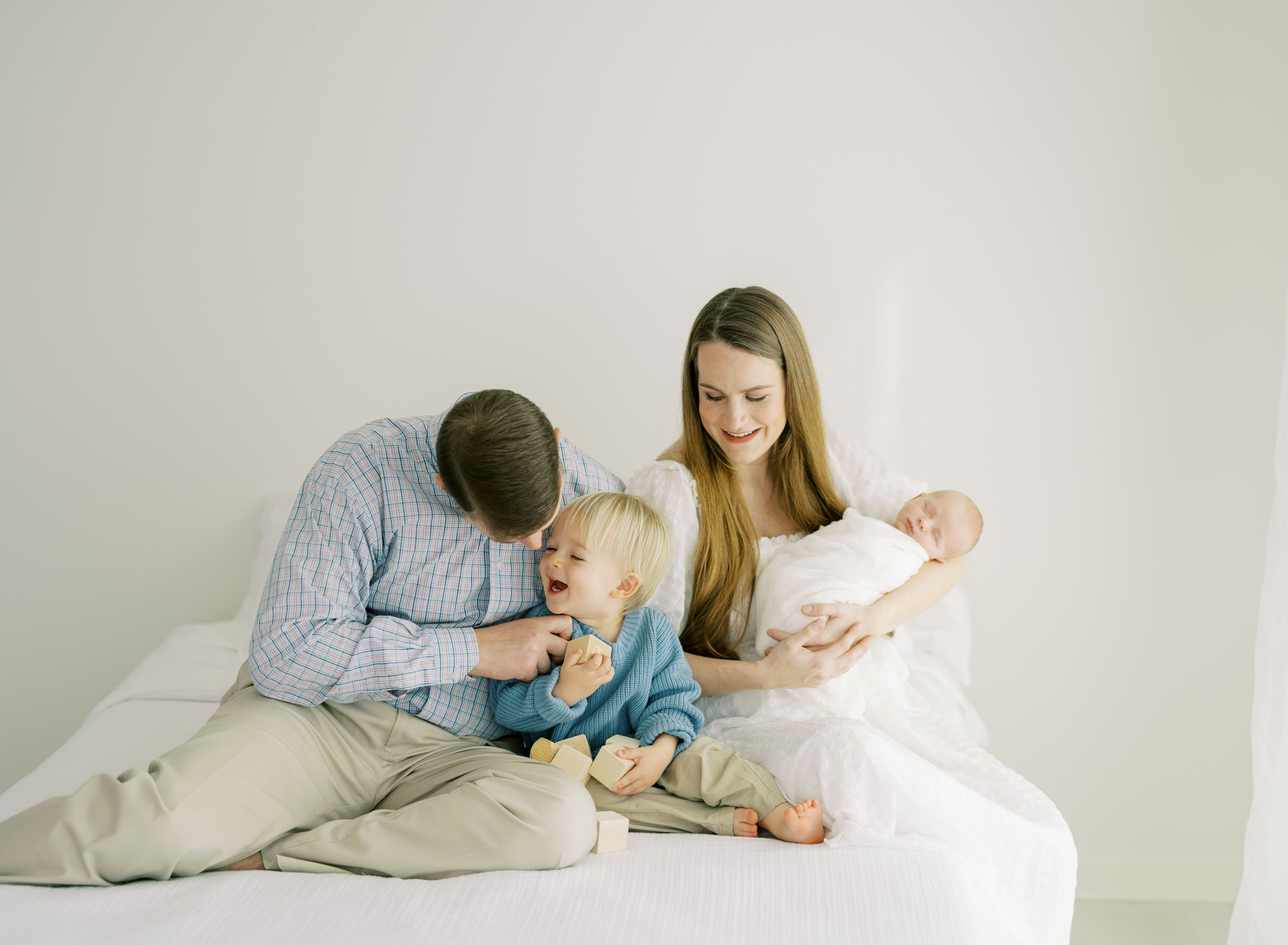 family of 4 playing on bed during studio newborn photoshoot