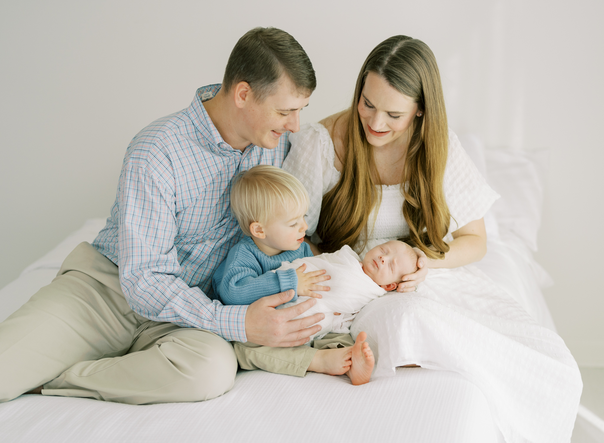 family of 4 interacting on bed during studio newborn photoshoot