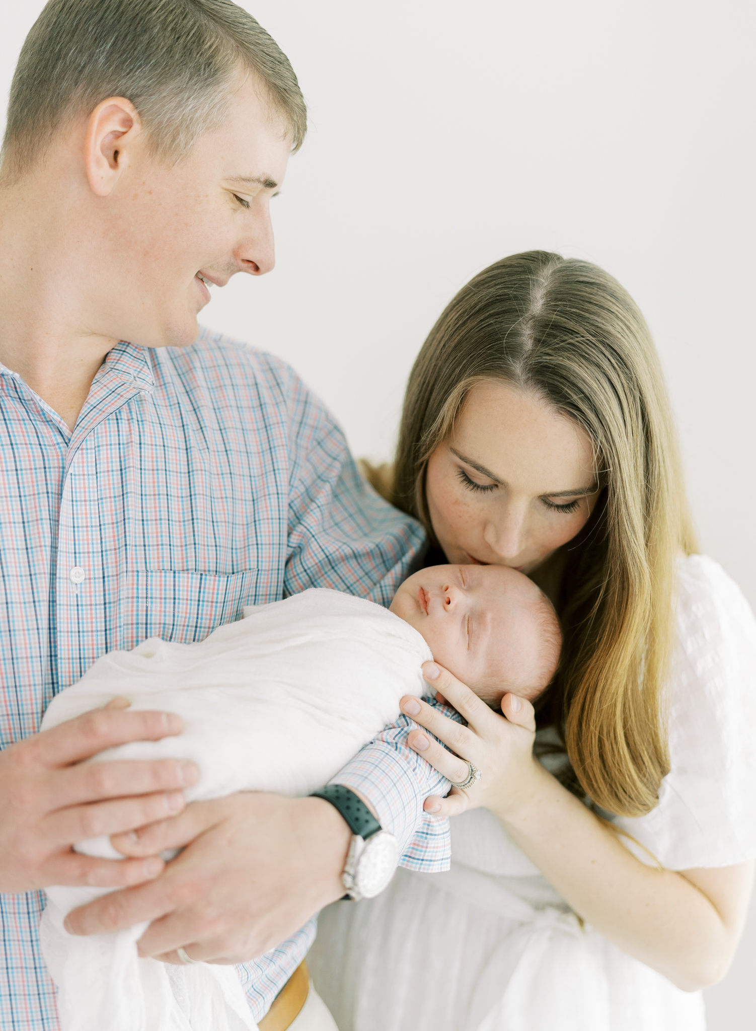 mom kissing newborn in dad's arms