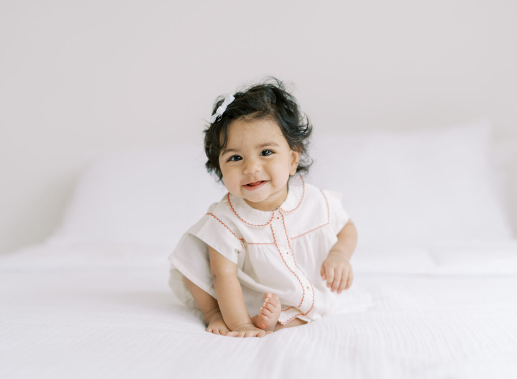 6 month baby girl smiling on a bed in a clean white studio for a natural portrait.