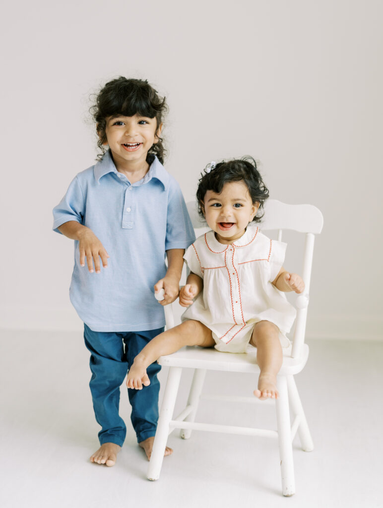 6 month baby girl with big brother smiling on a white chair for clean, bright, and natural portrait in Atlanta photography studio.