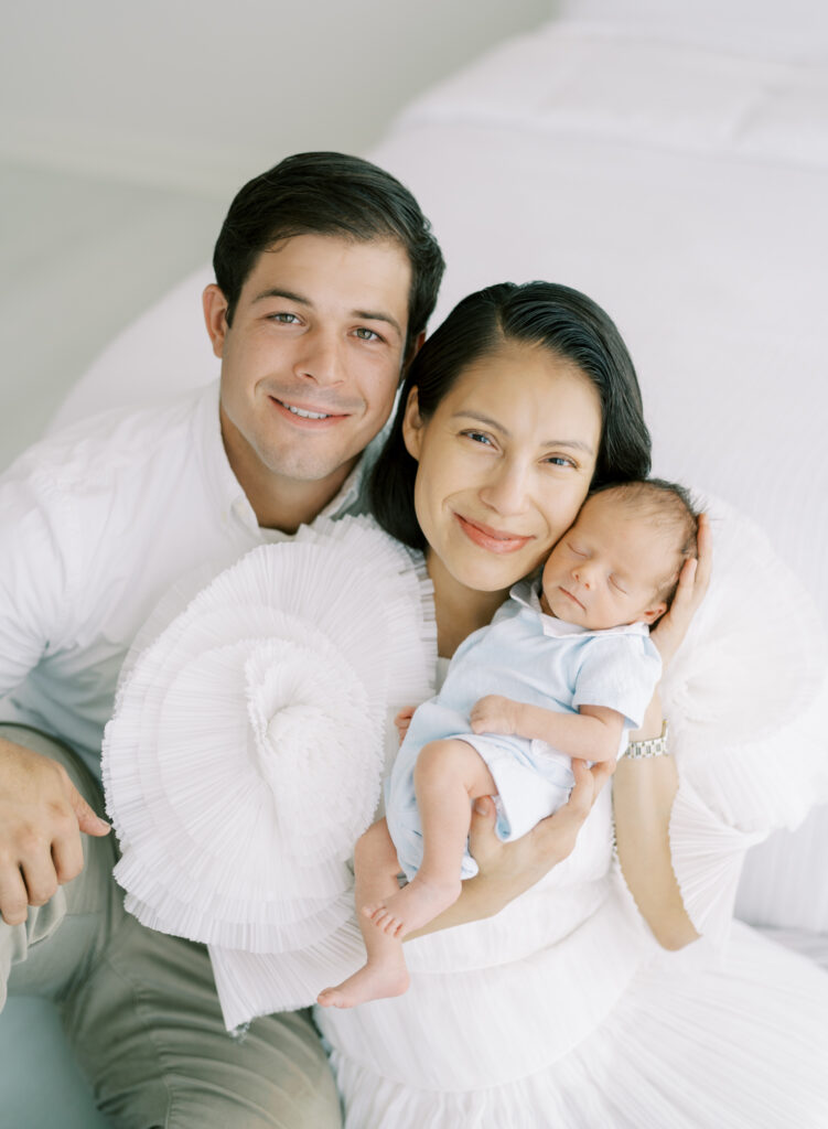 Happy mom and dad smiling with newborn son in clean and natural family photoshoot.