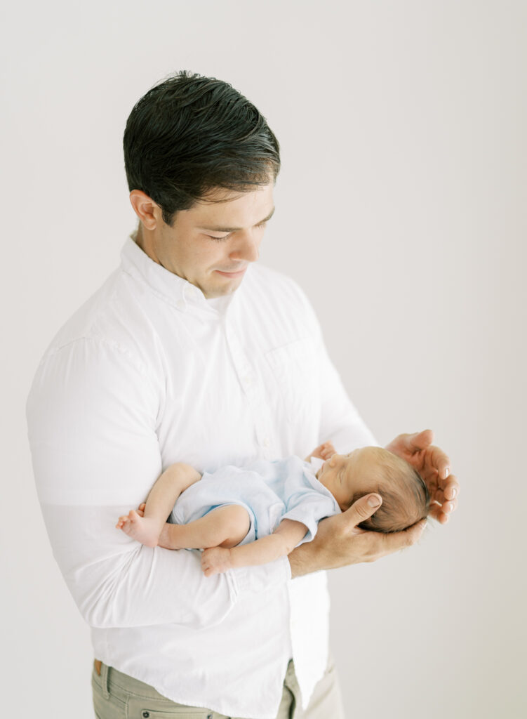 Dad holding newborn son in his hands and cupping his head. 