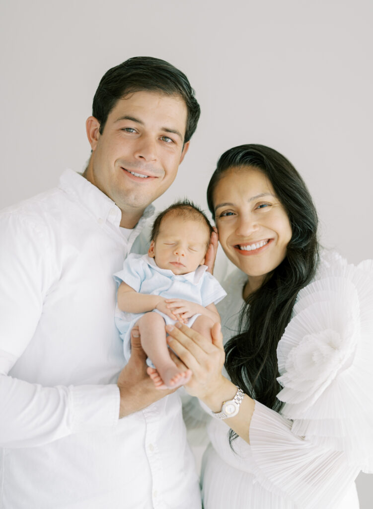 Happy new parents holding newborn baby up to their faces in clean white studio portrait in cumming ga. 