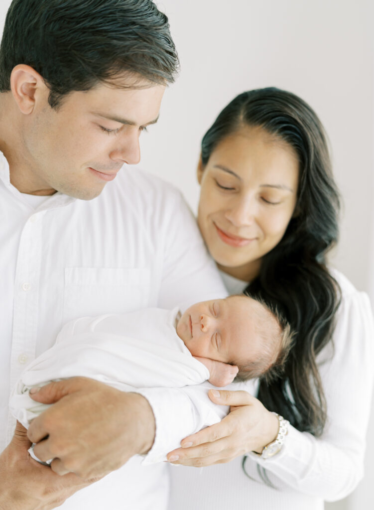 Luminous portrait of family holding newborn son in Cumming, GA photography studio.