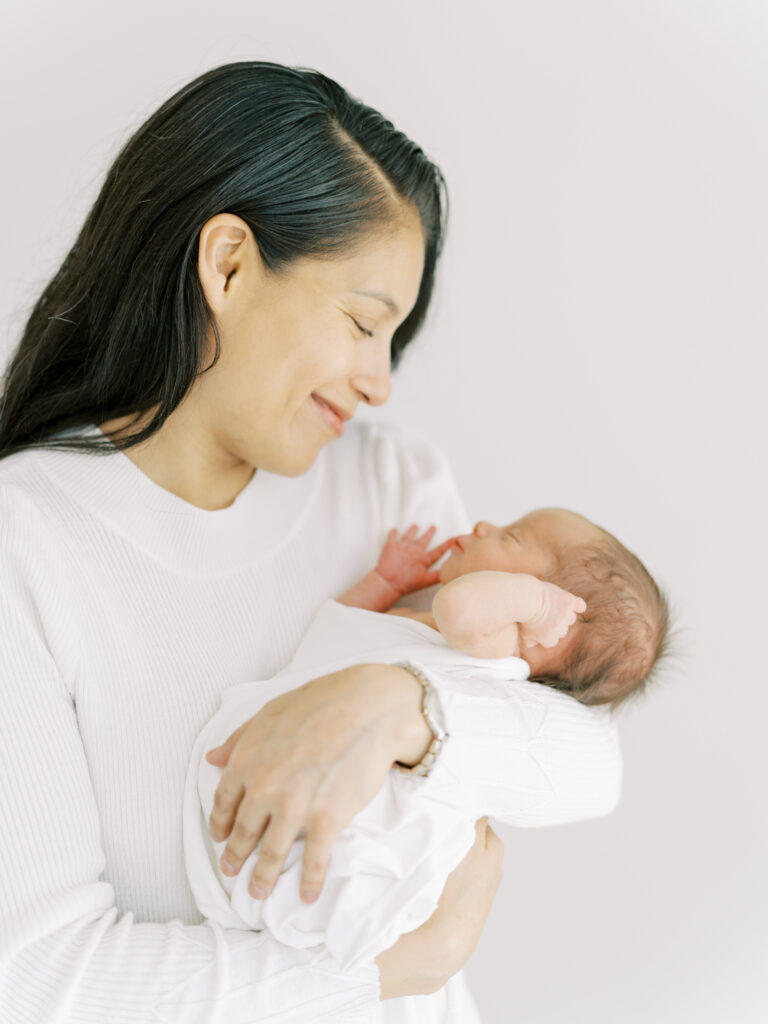 New mom holding newborn son as he stretched in natural light photography studio in Cumming, GA.