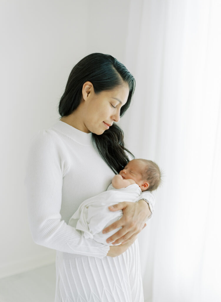 New mom holding son in natural light photography studio for natural newborn photos. 