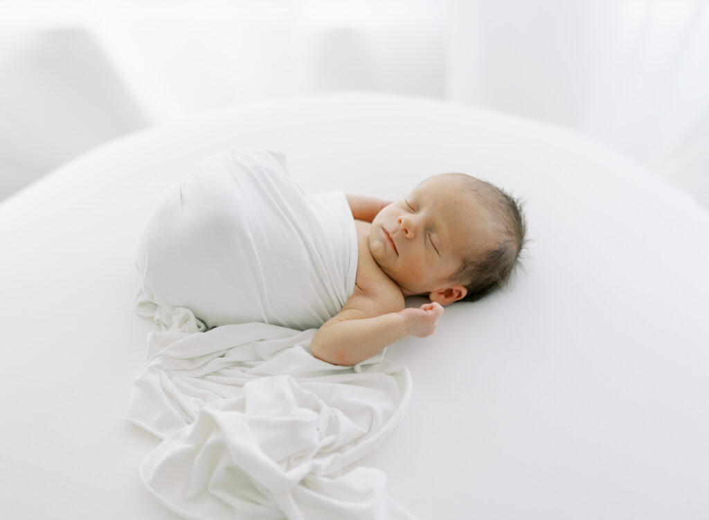 Newborn baby wrapped in a white swaddle on a white blanket for a clean and natural newborn photo in Cumming, GA.
