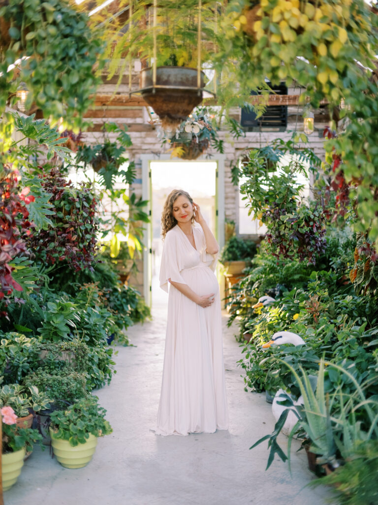 Pregnant woman in a long flowy dress surrounded by plants