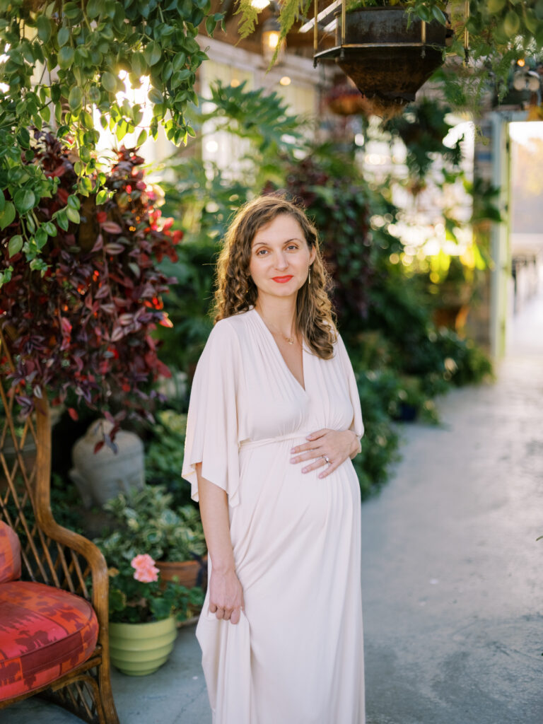 Pregnant woman in a long flowy dress surrounded by plants